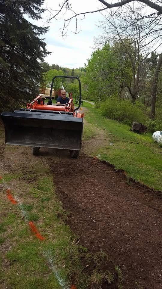Compact loader working on a stripped and graded area beside a lawn